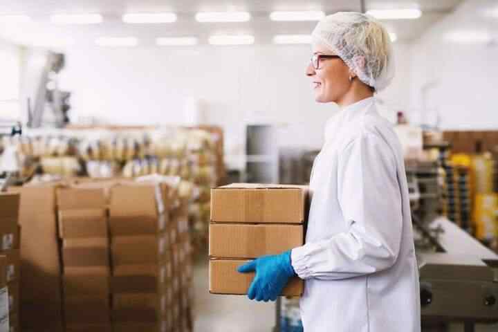 Young beautiful cheerful female worker is carrying a stack of bo Young beautiful cheerful female worker is carrying a stack of boxes to cargo room.